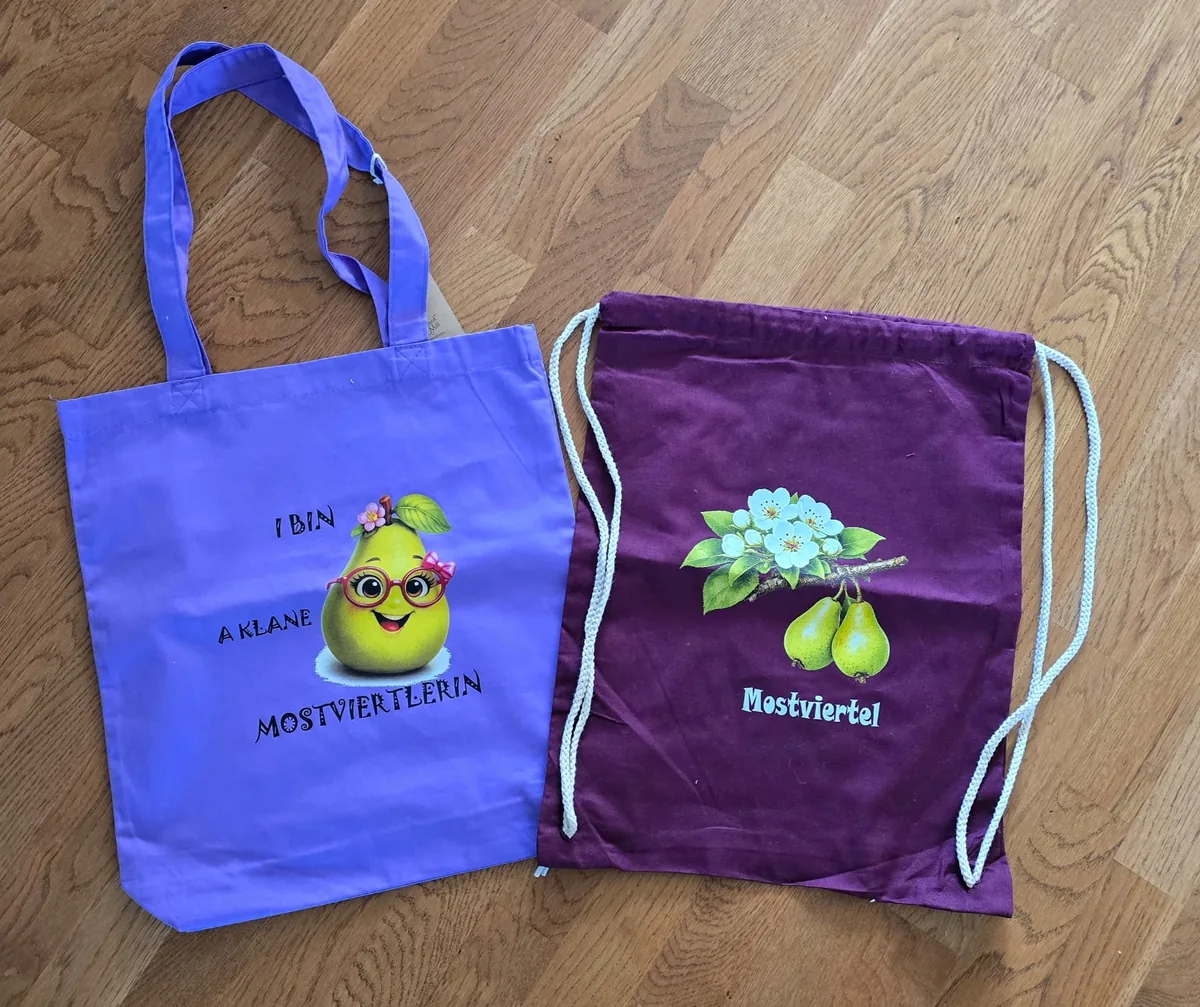 Lila Baumwolltasche und weinroter Turnbeutel mit Mostviertler Birnen- und Blütenmotiv