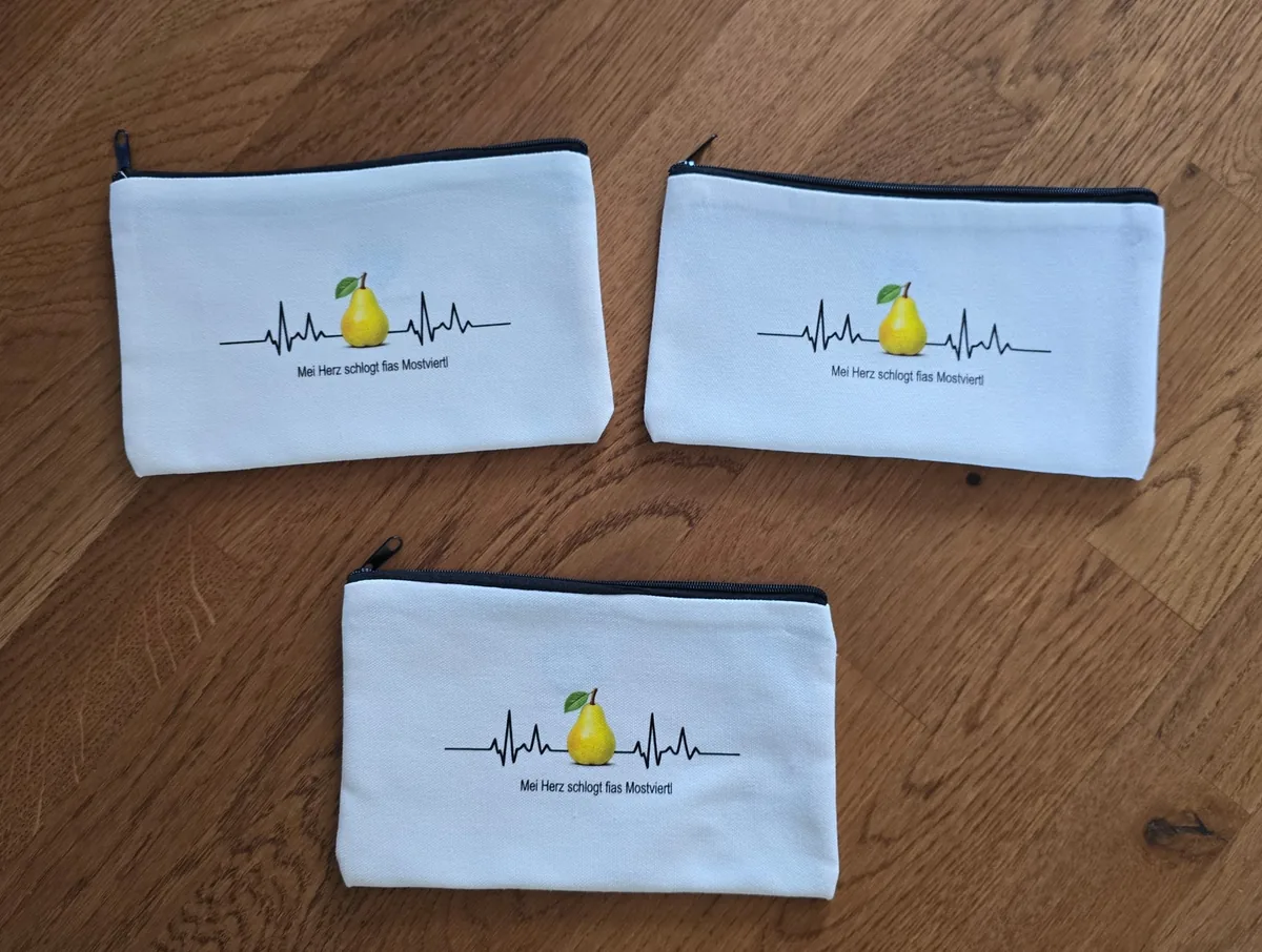 Drei weiße Reißverschlusstäschchen mit EKG-Herzschlaglinie und Mostviertler Birne